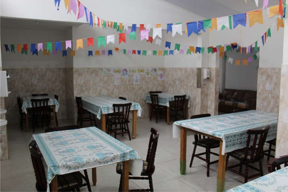 Refeitório do Cantinho com mesas de toalha xadrez e bandeirinhas de festa junina no teto